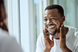 a-black-man-looking-in-the-bathroom-mirror-during-his-morning-routine-at-home.-Skin,-head-and-reflection-with-a-handsome-male-grooming-for-wellness-or-natural-care