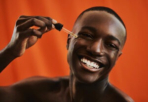 handsome-young-black-man-happily-applies-moisturising-serum-to-his-face,