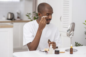 A man gently applies cream to his face, focusing on his cheeks and forehead.