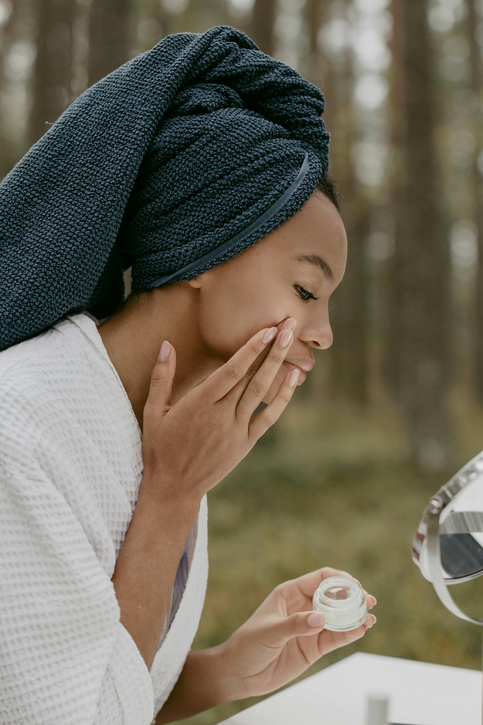 A woman in a bathrobe examining her reflection in a mirror, focusing on her face.