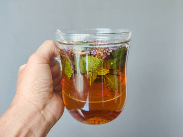 Close-up POV shot of unrecognizable woman drinking a glass of minty herbal tea, with a gray background wall