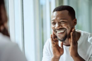 Beauty, face and skincare with a black man looking in the bathroom mirror during his morning routine at home. Skin, head and reflection with a handsome male grooming for wellness or natural care